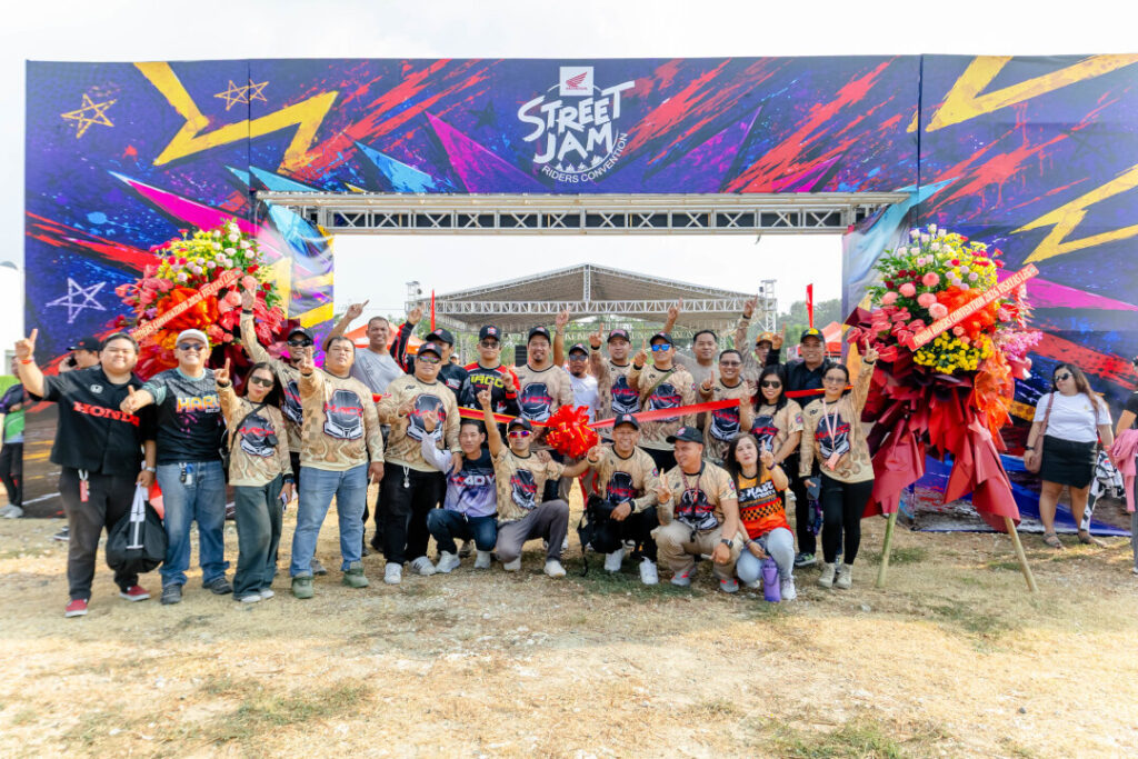 A large group of club members posing with a red ribbon for the opening ceremony under the colorful entrance arch of the Honda Riders Convention Visayas.