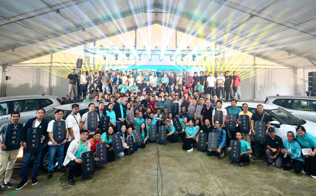 Hundreds of new Green GSM Philippines driver partners gather under a brightly lit tent at night for a group photograph, holding commemorative certificates to mark the official vehicle handover ceremony.