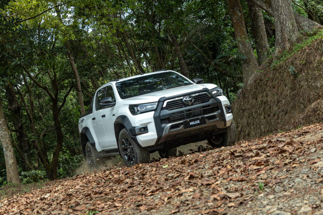 A white Toyota Hilux driving up a steep, leafy dirt slope, highlighted during the Toyota promos September 2026.