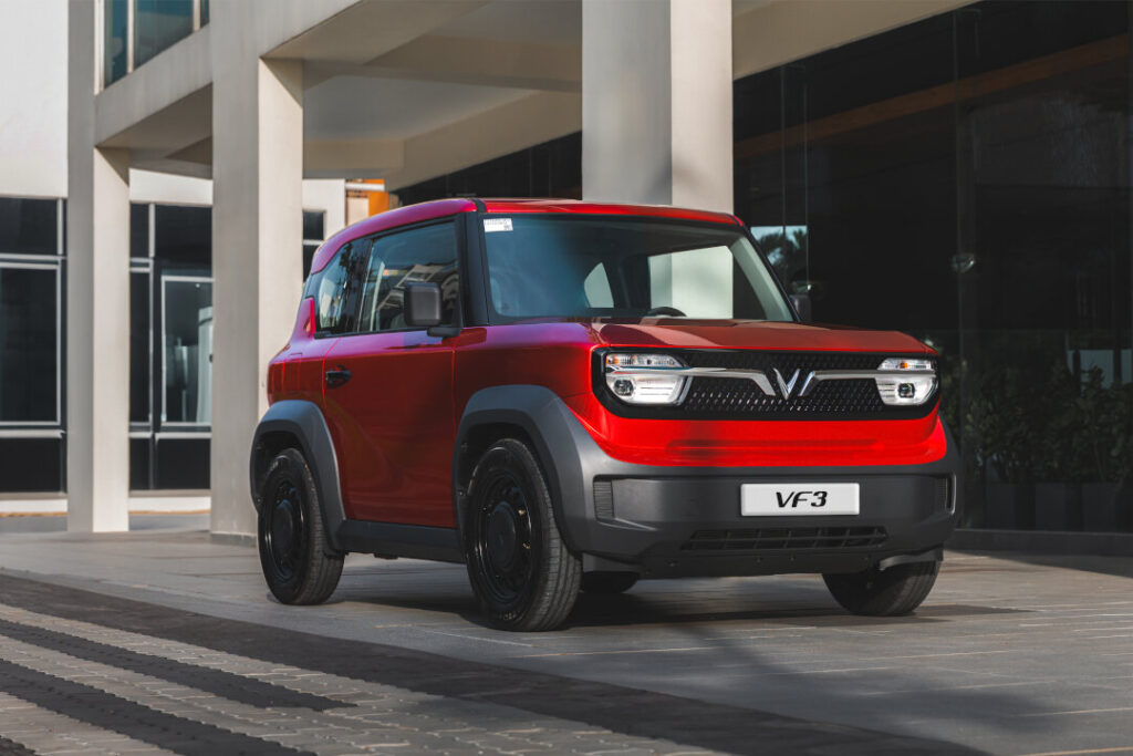 A vibrant red VinFast VF3 electric mini-SUV, available soon at VinFast EV showrooms Philippines, parked outside a modern commercial building with large concrete pillars.