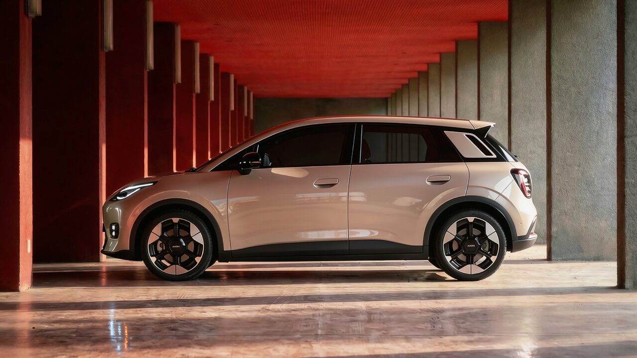 A side profile shot of a gold GAC Philippines AION UT electric hatchback parked between modern, geometric concrete pillars with an orange ceiling.