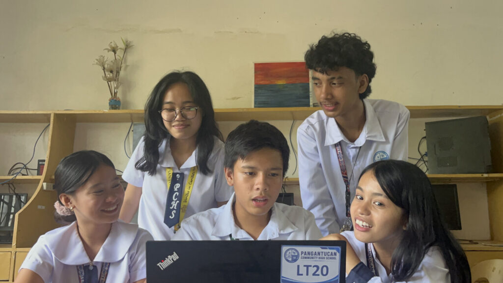 Five students at Pangantucan Community High School in uniform smile and collaborate while using a computer received through the Caltex laptop donation Bukidnon.