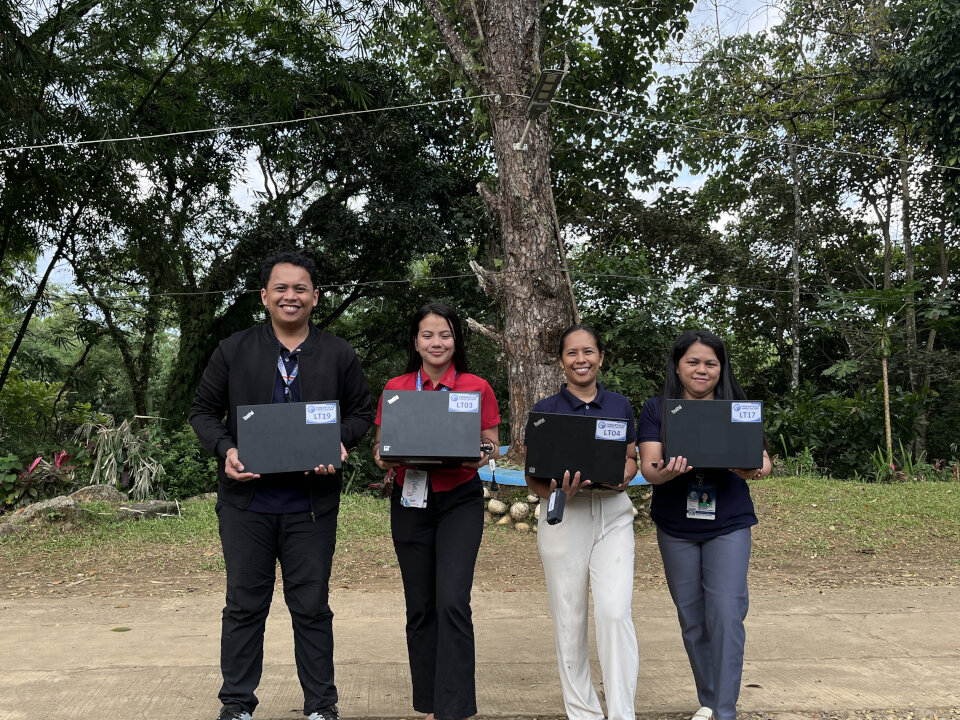 Four staff members holding laptops and posing outdoors to signify the successful implementation of the Caltex laptop donation Bukidnon to bridge the digital divide.