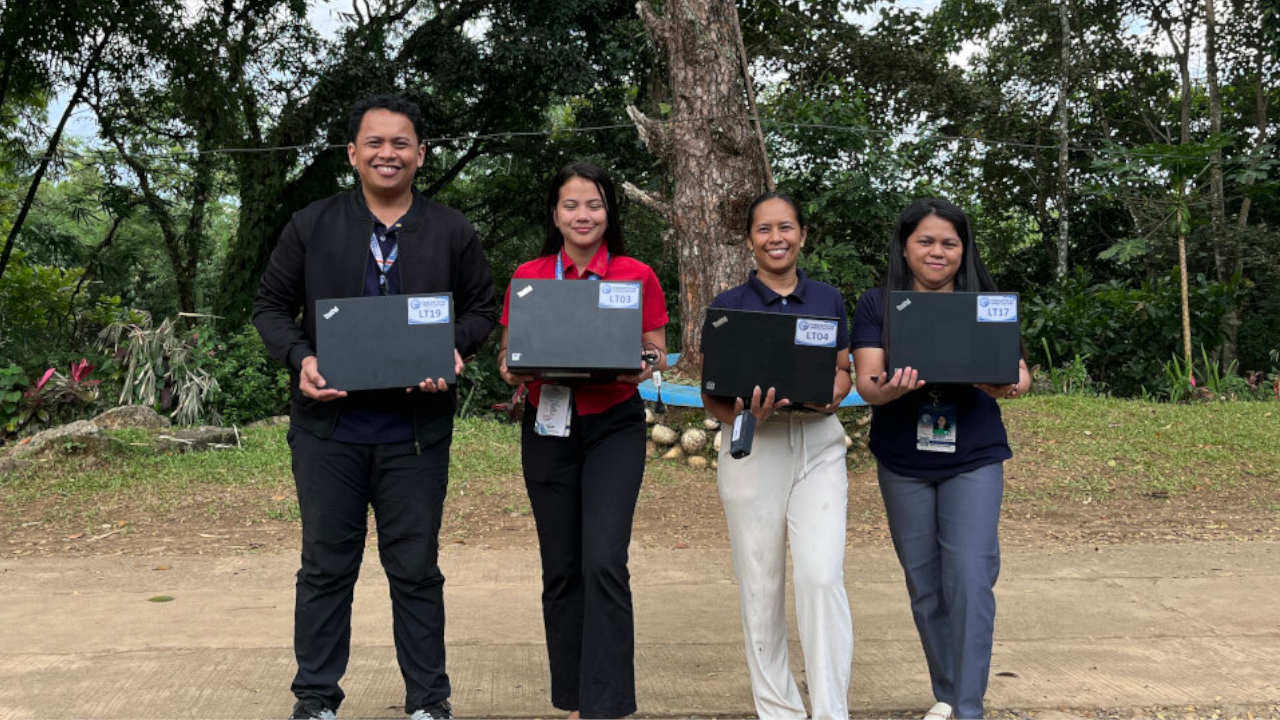 Close up view of four staff members holding laptops and posing outdoors to signify the successful implementation of the Caltex laptop donation Bukidnon to bridge the digital divide.